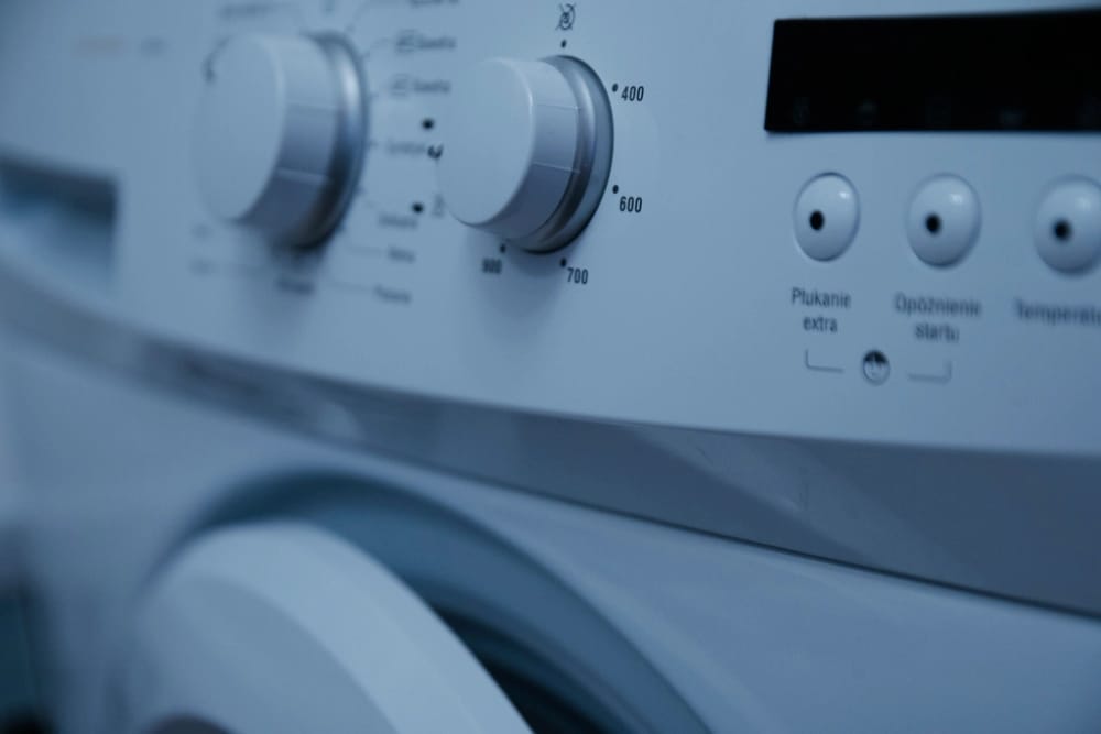 Close detail of a washing-machine control panel with programme dials and buttons.