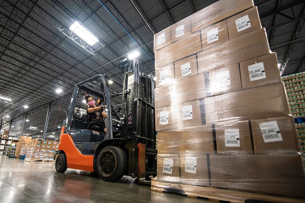 A forklift operator moving a wrapped and labelled pallet through a distribution warehouse.